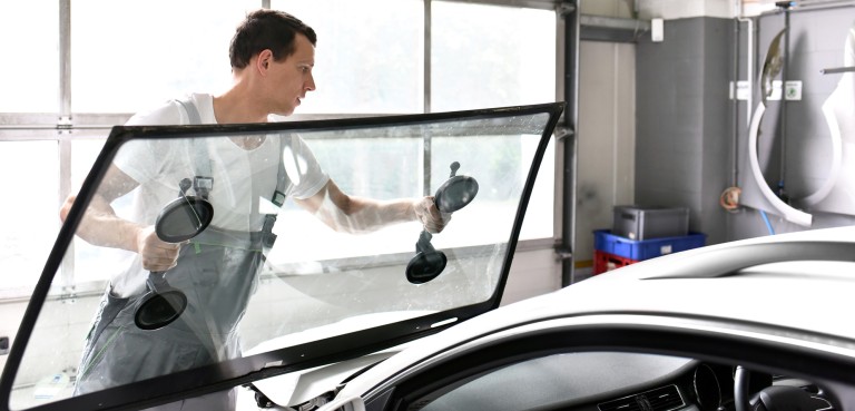 монтаж стекол Young mechanic in car workshop changing the windscreen of a car
