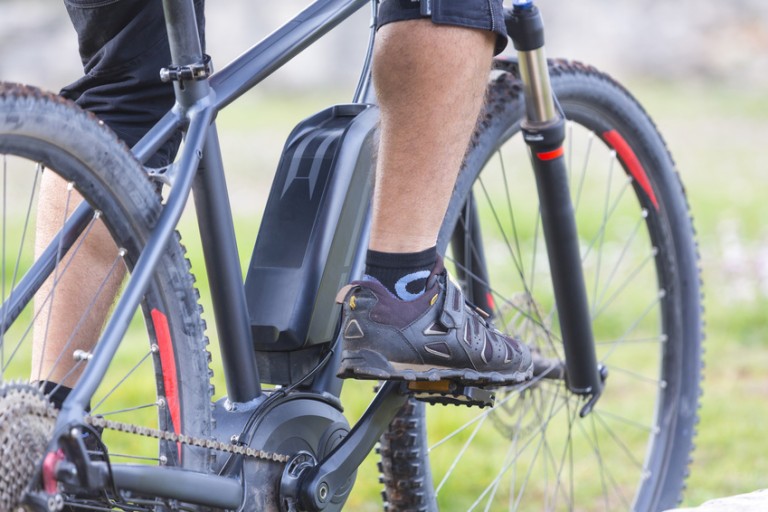 Электрические велосипеды Legs and sneakers on the pedals of a black e-bike
