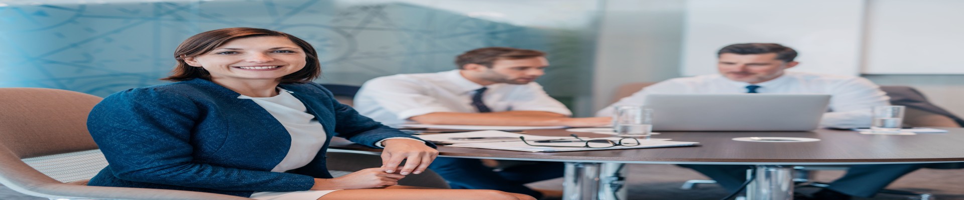 Portrait of a smiling young businesswoman sitting at a table with colleagues working in the background