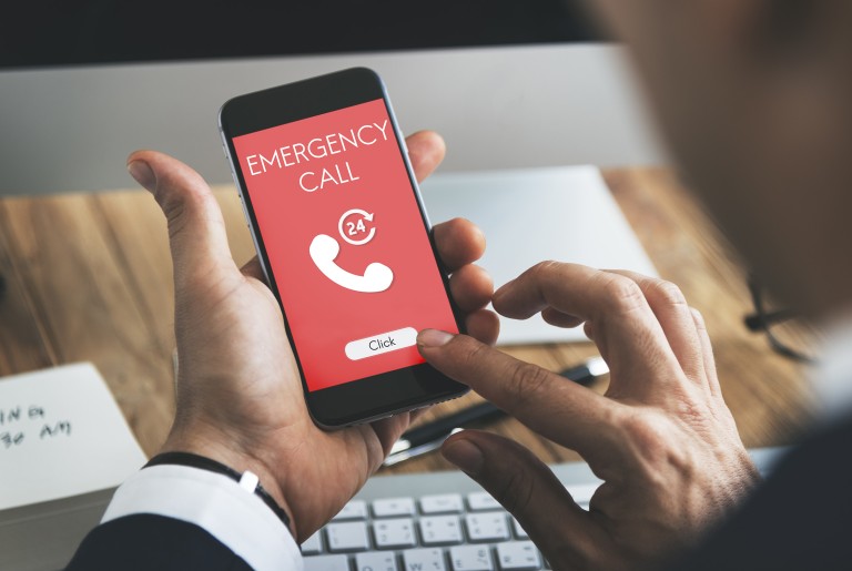 Токсикологический центр Hand holding a smartphone with a red-white colored display showing the letters emergency call
